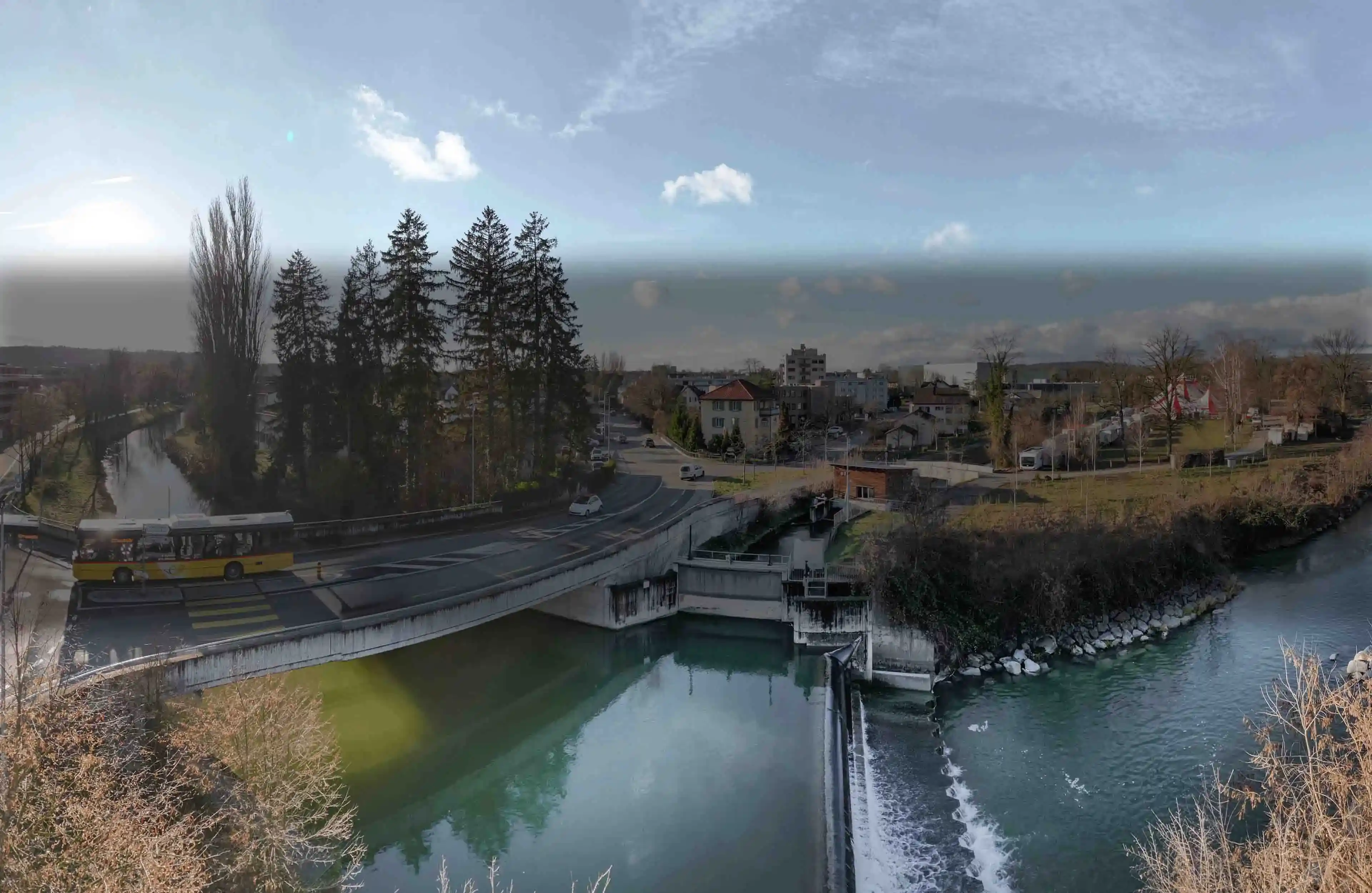 Fluss mit einem Wasserkraftwerk, daneben fährt ein Postauto über eine Brücke
